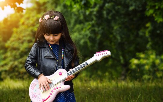 fillette en veste en cuir qui joue guitare dans un champs