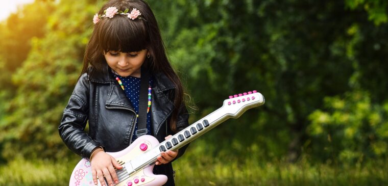 fillette en veste en cuir qui joue guitare dans un champs