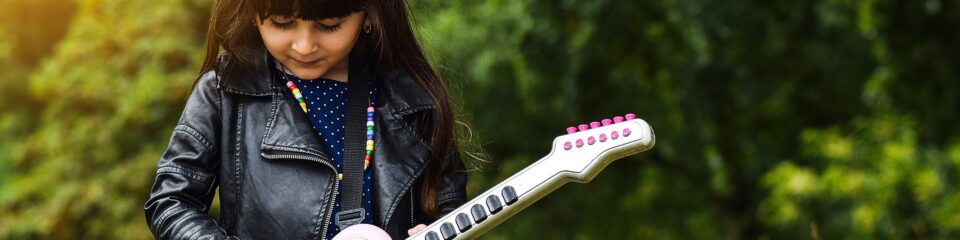 fillette en veste en cuir qui joue guitare dans un champs