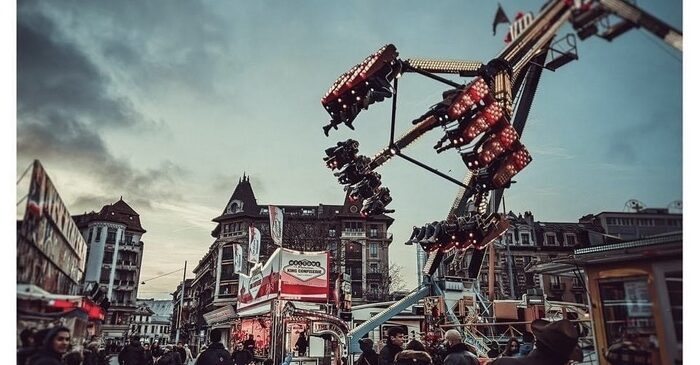 manèges fête foraine avec bâtiments en fond et piétons dessous