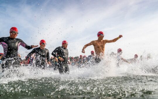 hommes courent dans l'eau avec combiinaison et bonnet de bain rouge