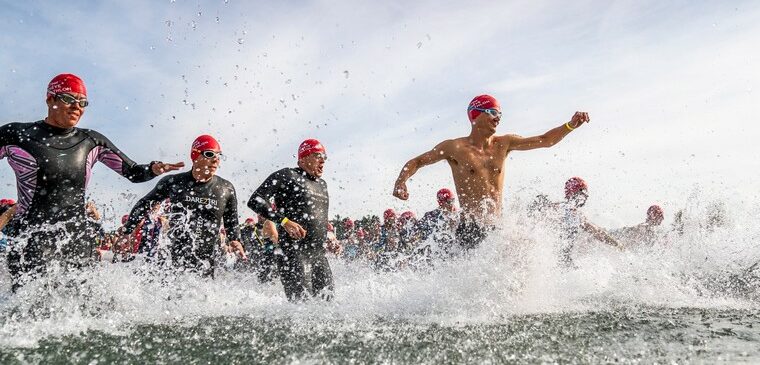 hommes courent dans l'eau avec combiinaison et bonnet de bain rouge