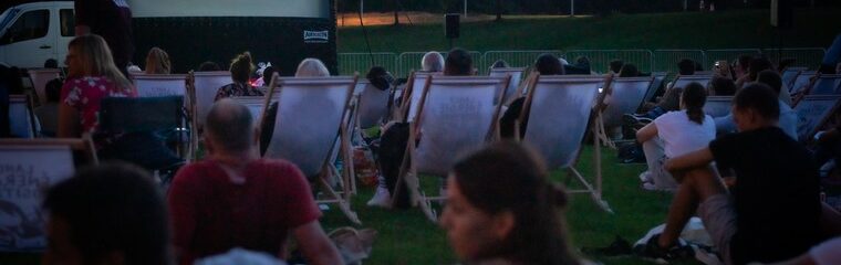 peronnes dans des transats et assis dans l'herbe devant écran cinéma en plein air