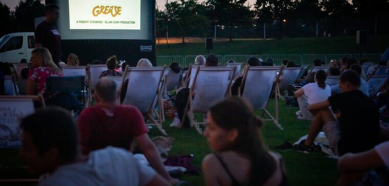 peronnes dans des transats et assis dans l'herbe devant écran cinéma en plein air