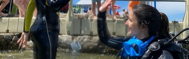 une femme en combinaison de plongée dans l'eau tape dans la main d'un enfant debout dans l'eaun